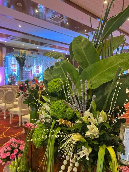 A large, stunning floral arrangement with tropical leaves that frames the view of the main stage, adding depth and grandeur to the space.
