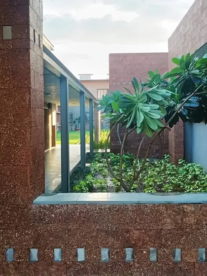 A view through a window-like opening at the Bagchi Karunashraya hospice in Bhubaneswar. The laterite stone walls frame a small, private courtyard, creating a moment of quiet connection with nature.
