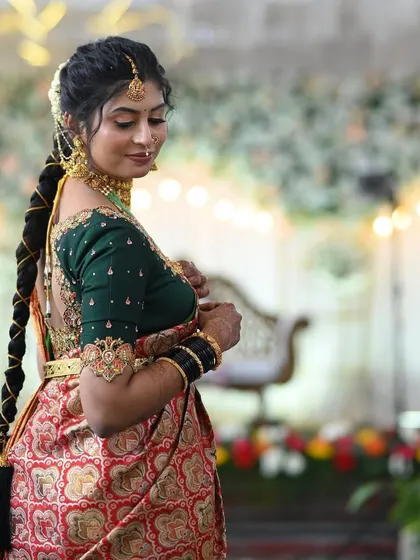 A side profile of a bride showing her traditional braided hairstyle and the intricate embroidery on the sleeve of her dark green blouse.