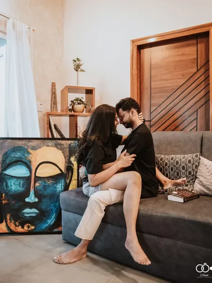 An intimate portrait of the couple on a sofa, their faces close, with a striking piece of Buddha art beside them, adding a serene and artistic touch.