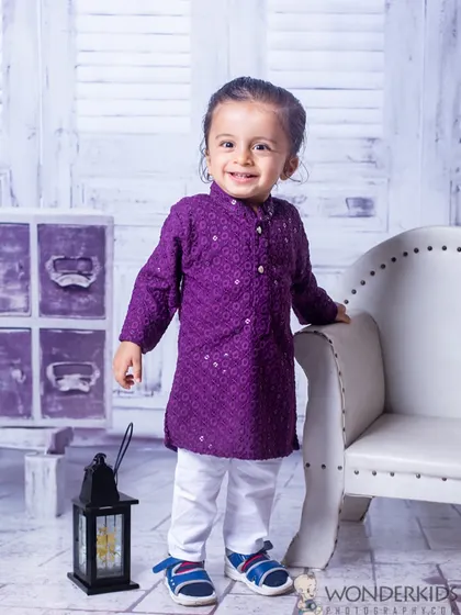 A little boy dressed in a smart purple kurta, looking very dapper for his photoshoot. The simple, clean background helps his personality and stylish outfit stand out.