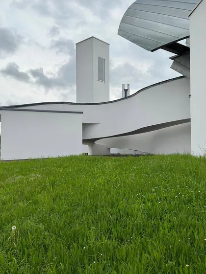 The building's form seen against a grassy landscape. The architecture has a dynamic, almost animated quality, with its various volumes colliding and intersecting.