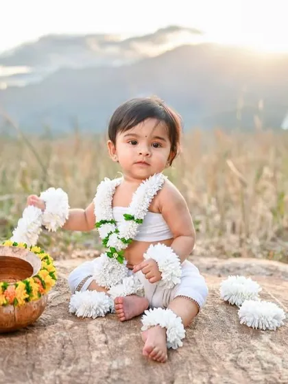 An outdoor shoot with a traditional touch. This baby is sitting by a serene waterfall, creating a beautiful contrast between the natural environment and the simple, traditional attire.