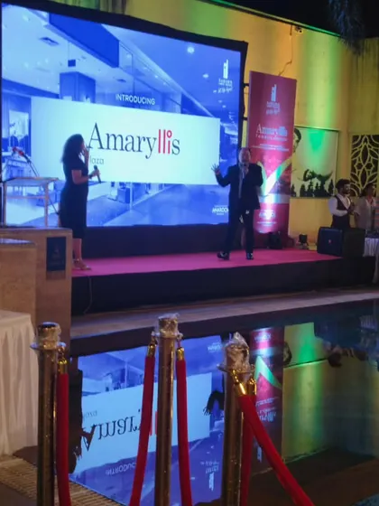A poolside product launch for 'Amaryllis'. The setup includes a stage with a large LED screen for the presentation, professional lighting, and a roped off VIP area.
