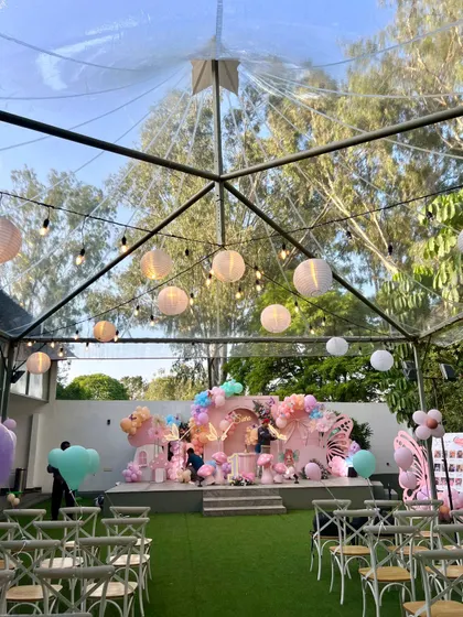 An outdoor fairy party setup under a clear-top tent. This allows us to enjoy the natural surroundings while having a defined and beautifully decorated event space.