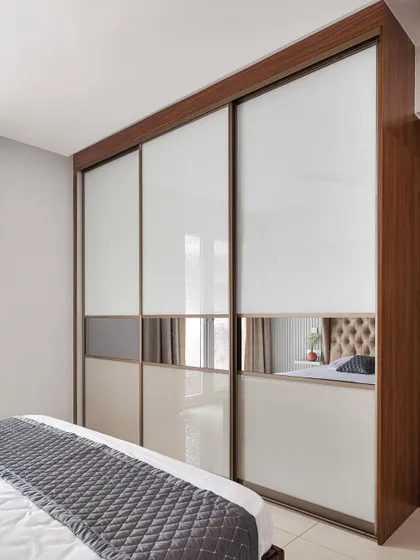 A full-height, floor-to-ceiling sliding wardrobe with Aristo doors. The design combines back-painted glass with a central tinted mirror panel, which reflects the bedroom and makes the space feel larger and brighter.