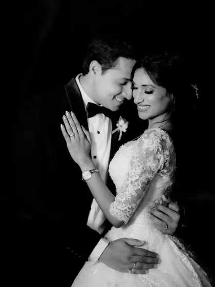 A joyful black and white portrait of the couple. The image captures their smiles and the classic elegance of their wedding attire against a dark backdrop.
