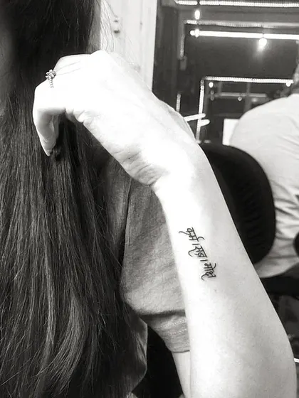 A black and white shot of a delicate 'Ant asti prarambh' script tattoo on the wrist, showcasing its elegant placement.