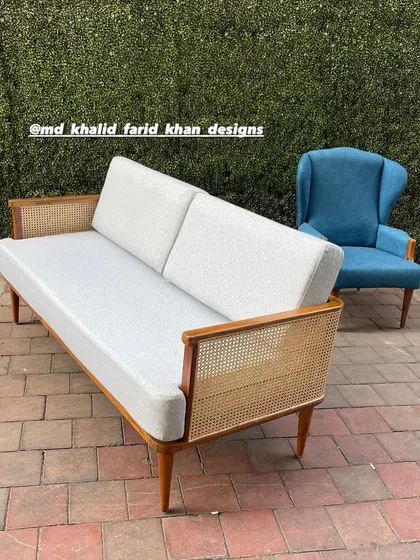A mid-century modern sofa with a cane-panelled back, paired with a vibrant blue wingback chair.