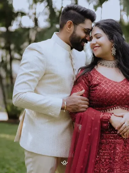 A happy couple in red and white engagement outfits, sharing an intimate moment in a garden.