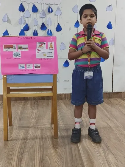 A UKG student confidently presents his project on different modes of transport, demonstrating early research and public speaking skills.