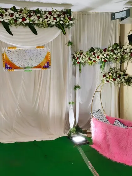 An elegant and simple naming ceremony setup. It features a backdrop with a floral border and a modern metal cradle decorated with pink fur.