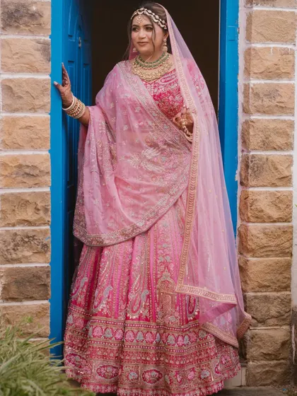 A beautiful bride framed by a vibrant blue doorway. The contrast of colors makes her pink lehenga pop, creating a striking and memorable bridal portrait.