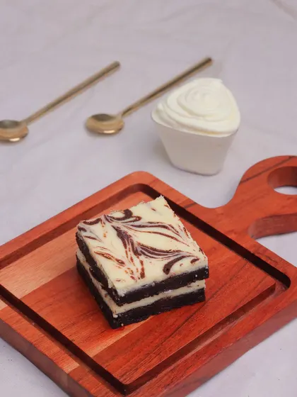 A single Cheesecake Brownie served with a side of whipped cream, a perfect pairing for this rich dessert.