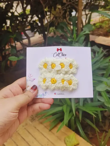 A pair of our adorable daisy hair clips, held up against a natural green background.