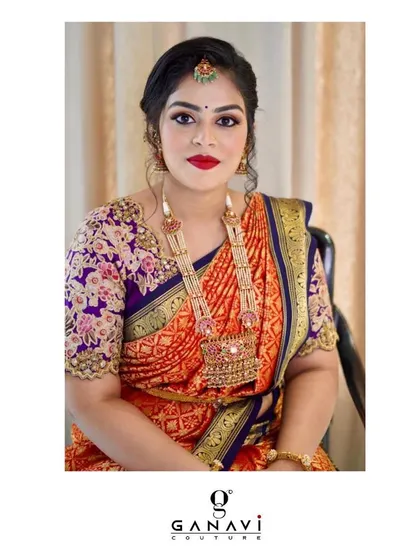 The gorgeous Swetha in our exclusively customized blouse. The intricate floral embroidery in purple and pink tones perfectly complements her vibrant orange and blue silk saree.