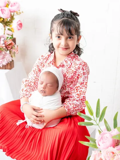 A proud big sister holds her newborn sibling for the first time in the studio. Sibling portraits are a beautiful way to welcome a new member to the family.