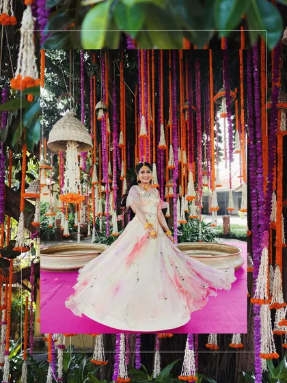The bride, a vision in her flowy dress, stands amidst a curtain of hanging marigold and mogra chandeliers, creating an ethereal and colorful backdrop.
