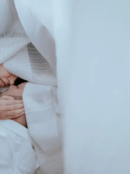 An intimate and artistic pre-wedding shot, with the couple wrapped in soft, white curtains. This style creates a dreamy and romantic atmosphere.
