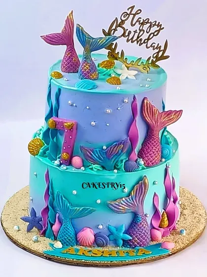 A beautiful two-tier mermaid cake combining chocolate and vanilla flavors. The aqua and lavender design is decorated with fondant mermaid tails, starfish, and seashells for a 7th birthday.