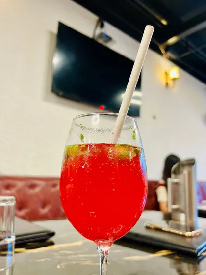 A vibrant red mocktail, possibly watermelon or strawberry, served in a wine glass. The bright color stands out against the dark marble table, making for a striking and appealing image.