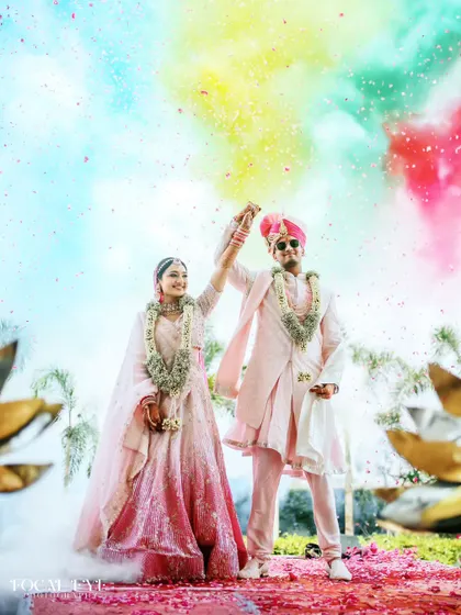 A joyful Varmaala moment, with the couple raising their hands in celebration under a burst of colored powder. We capture the energy and excitement of your big day.