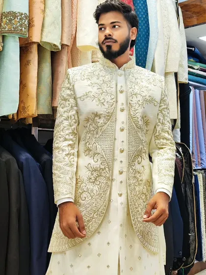 A client wearing a hand-embroidered open sherwani in off-white. The gold embroidery adds a touch of opulence to the elegant outfit.