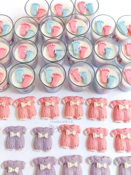 A collection of baby shower return gifts, including layered votive candles with baby feet and colorful baby onesie wax sachets.