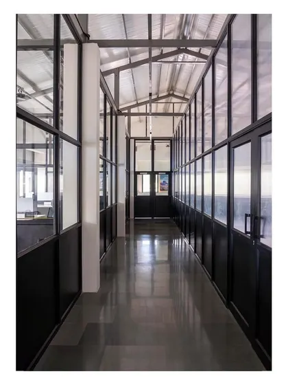 Another view of the office corridor, highlighting the polished concrete floors and the lofty exposed metal roof, which contribute to the space's clean, industrial aesthetic.