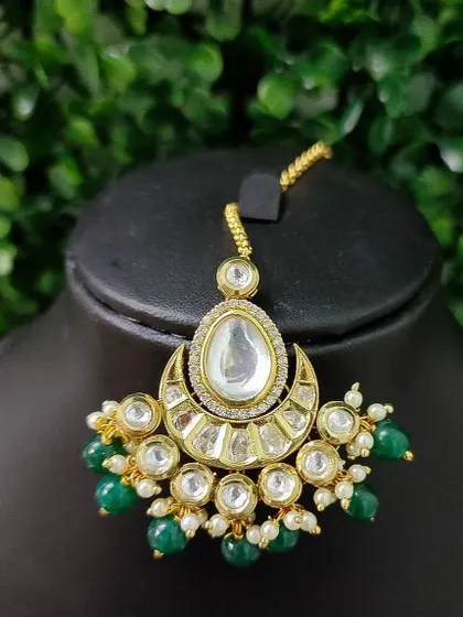 A beautiful kundan maang tikka with a large central polki stone and green bead drops. The crescent shape is a classic bridal choice.
