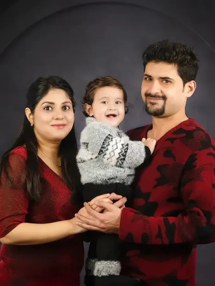A happy family of three, dressed in matching red and black tones, smiles warmly for the camera. A beautiful portrait against a dark, moody backdrop.