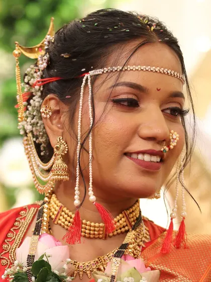 A close-up of a bride in a red Nauvari, her smile lighting up her face. The makeup features a warm, rosy blush and a perfectly matched lip color.