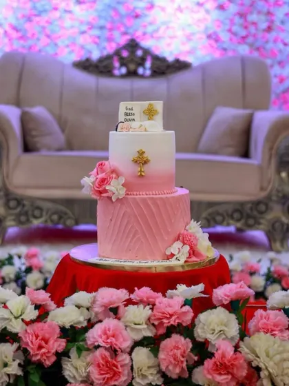 Celebrating baby Olivia's baptism with this two-tiered pink cake. The design includes a pink ombre top tier, a textured bottom tier, and is adorned with fresh flowers and gold crosses.