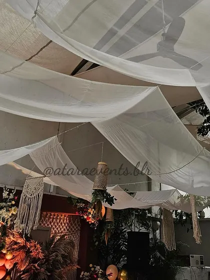 The ceiling decor of a boho-themed event. Draped white fabric and macrame hangings create a soft, romantic, and free-spirited atmosphere.