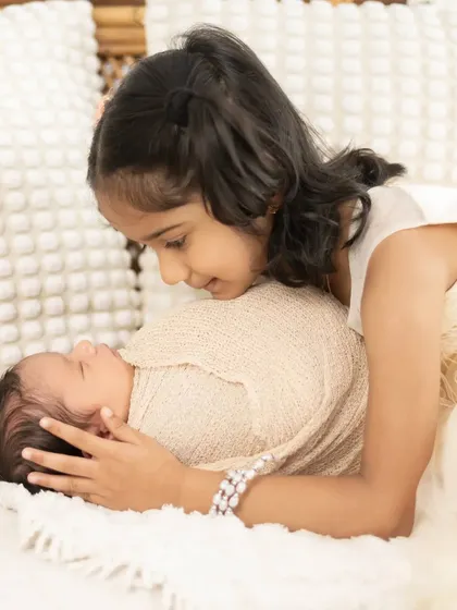 A close-up of an older sister looking lovingly at her new baby sibling. We focus on capturing the gentle interactions and budding bond between them.