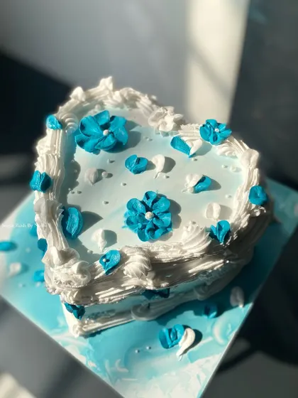 A vintage-inspired heart-shaped cake in shades of blue and white. The delicate floral piping gives it a charming and romantic feel.