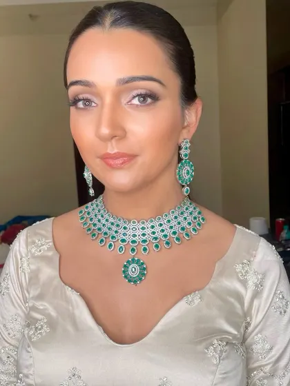 A divine Sangeet or Reception look in an all-white lehenga with stunning emerald jewelry. The makeup is clean with a focus on the eyes.