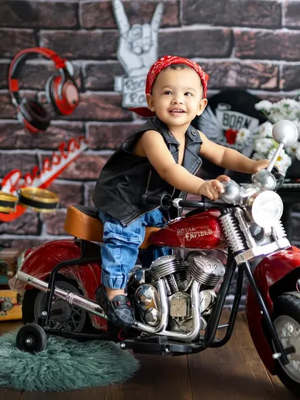 A future road king! This little biker looks right at home on a miniature motorcycle, complete with a red bandana and a leather vest.