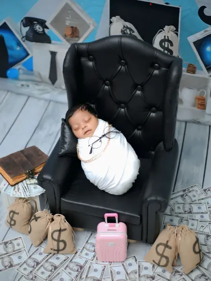 The 'Boss Baby' takes a seat in a miniature black leather armchair, surrounded by bags of money.