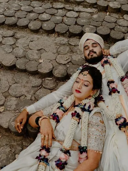 An artistic overhead shot of a newly married couple in traditional white attire, resting on stone steps after their ceremony. This creative angle captures a moment of quiet togetherness.