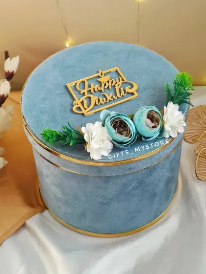 The closed view of our round velvet hamper box. The soft texture, gold trim, and floral accents make it a truly luxurious gift.