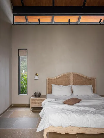 This bedroom at Grove House features a simple, elegant rattan headboard and clerestory windows that bring in light while maintaining privacy. The use of natural materials and textures creates a calm and restful environment.