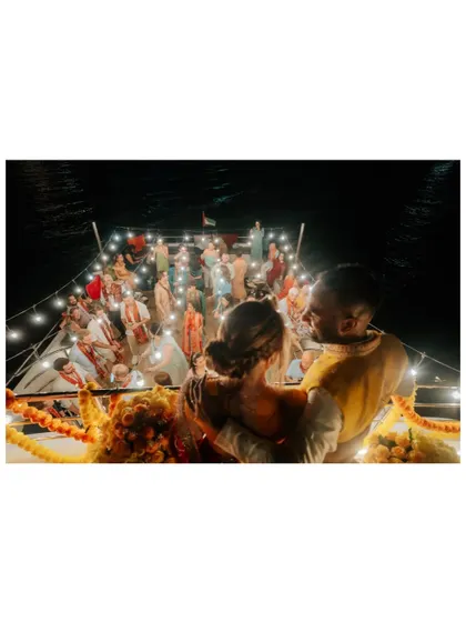 An atmospheric shot of the couple looking out at their party from the upper deck of the yacht, surrounded by lights.