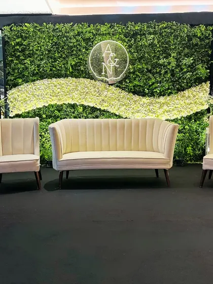 A modern reception stage featuring a living wall of lush greenery, a custom neon monogram, and elegant, contemporary seating for the couple.