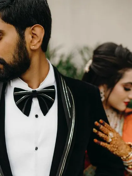 A modern couple's portrait focusing on the groom's sharp attire, with the bride creating a soft, romantic element in the background.