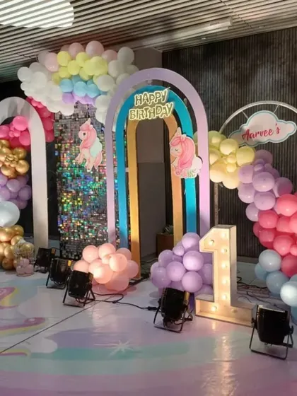 The full view of the unicorn first birthday stage, showing the layered backdrops, flowing balloon clouds, and a light-up number one.