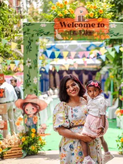 A happy welcome to the farm! The birthday girl and her mom pose at the entrance, which features a custom arch, colorful bunting, and fun scarecrow cutouts.
