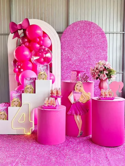 This Barbie theme is all about the glamour of pink. The setup includes a glittery pink backdrop, a neon number '4', and multiple pedestals to display the cake and other treats in style.