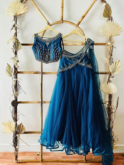 A teal blue Indo-Western lehenga with a fully beaded blouse and an attached dupatta. The unique silhouette makes it a modern and stylish choice.