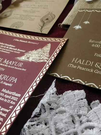 A detailed shot of our handmade jute invitation inserts. This card, for the Muhurtham ceremony, features traditional temple artwork with gold printing on a rich maroon background, blending rustic materials with cultural elegance.